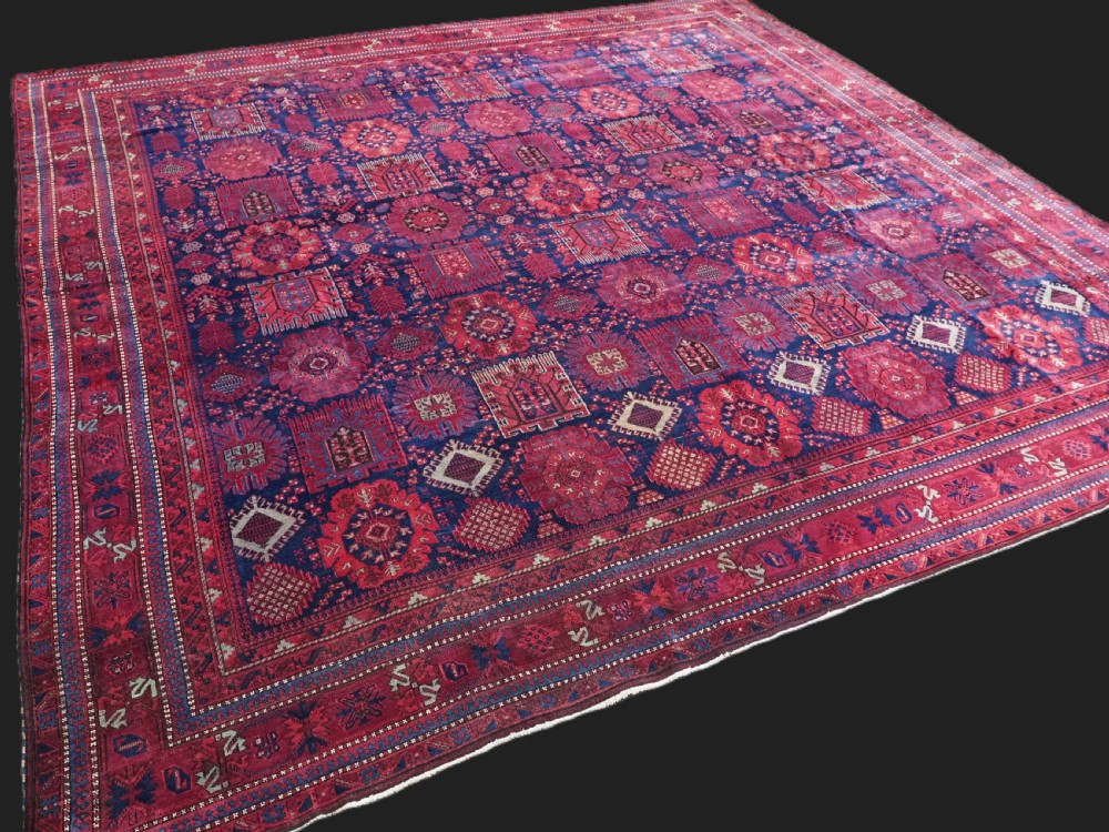 A large hand-knotted wool carpet featuring a repeating geometric medallion pattern in shades of crimson red, deep blue, and magenta. View II