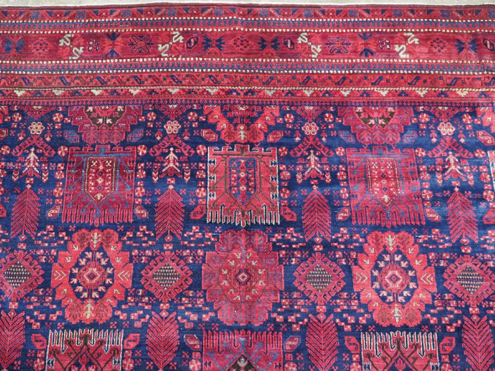 A large hand-knotted wool carpet featuring a repeating geometric medallion pattern in shades of crimson red, deep blue, and magenta. View VIII
