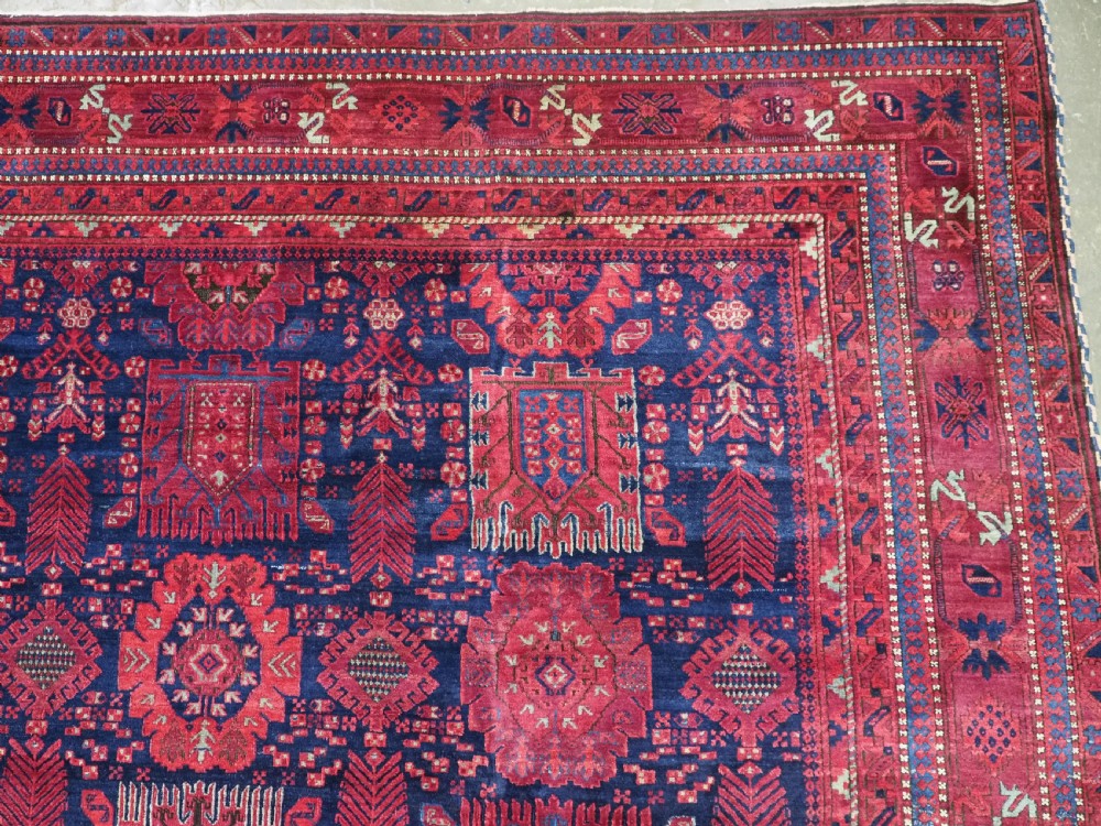 A large hand-knotted wool carpet featuring a repeating geometric medallion pattern in shades of crimson red, deep blue, and magenta. View IX