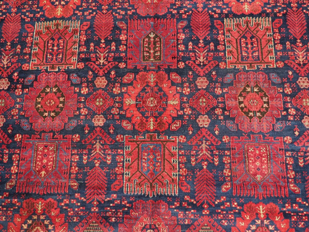 A large hand-knotted wool carpet featuring a repeating geometric medallion pattern in shades of crimson red, deep blue, and magenta. View X