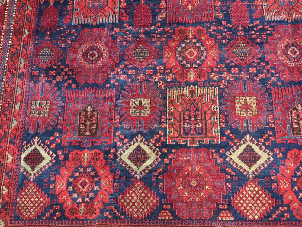 A large hand-knotted wool carpet featuring a repeating geometric medallion pattern in shades of crimson red, deep blue, and magenta. View XI