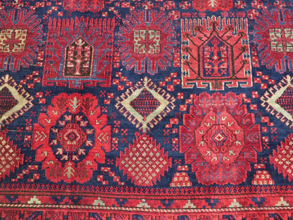 A large hand-knotted wool carpet featuring a repeating geometric medallion pattern in shades of crimson red, deep blue, and magenta. View XIII