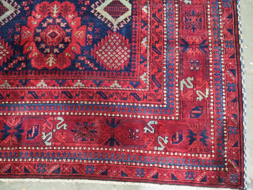 A large hand-knotted wool carpet featuring a repeating geometric medallion pattern in shades of crimson red, deep blue, and magenta. View XIV