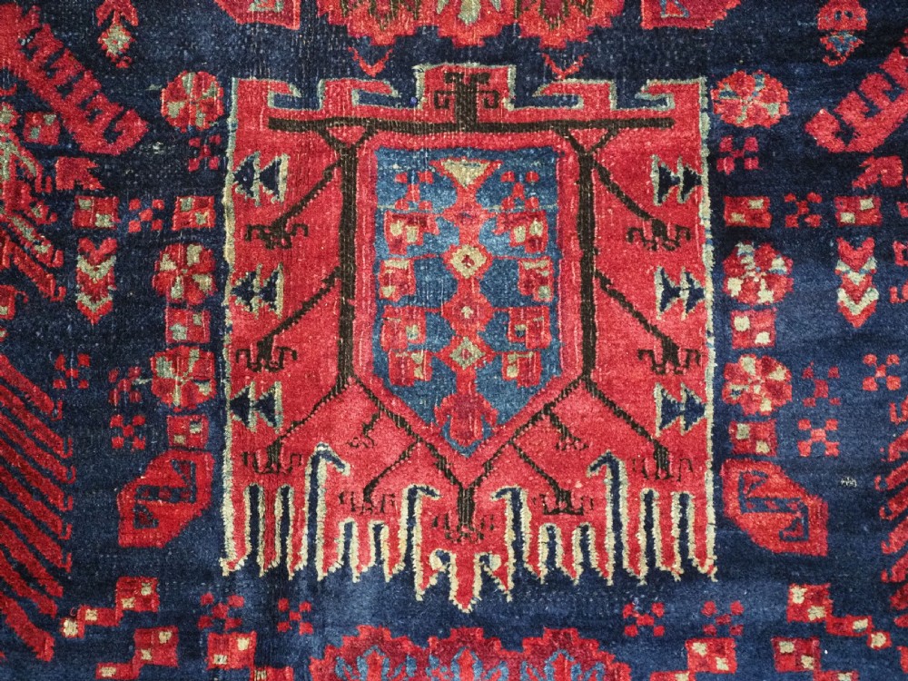 A large hand-knotted wool carpet featuring a repeating geometric medallion pattern in shades of crimson red, deep blue, and magenta. View XV
