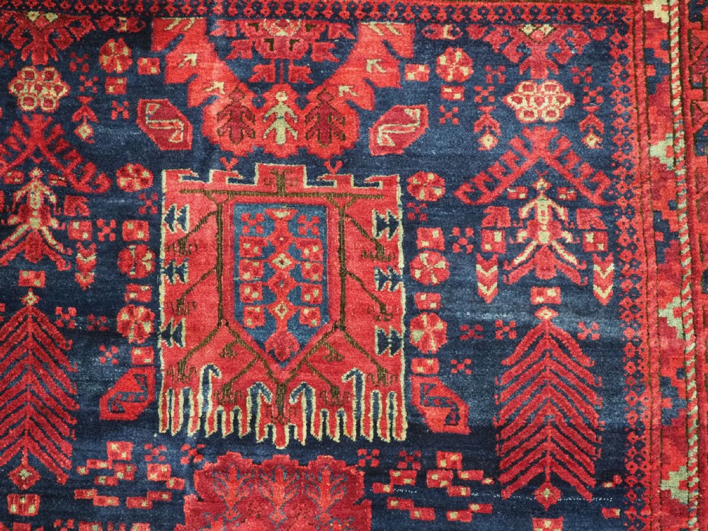 A large hand-knotted wool carpet featuring a repeating geometric medallion pattern in shades of crimson red, deep blue, and magenta. View XVI
