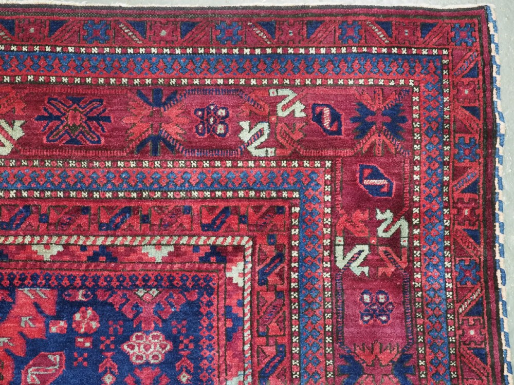 A large hand-knotted wool carpet featuring a repeating geometric medallion pattern in shades of crimson red, deep blue, and magenta. View XVII