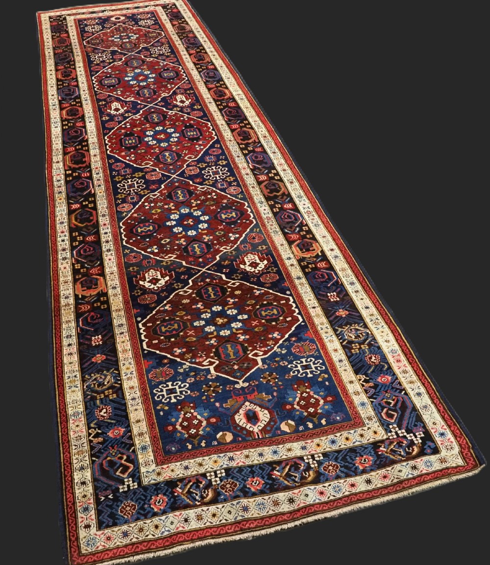 An antique hand-knotted Caucasian Alpan-Kuba runner rug featuring geometric diamond medallions in red and navy blue with detailed ivory borders. View II