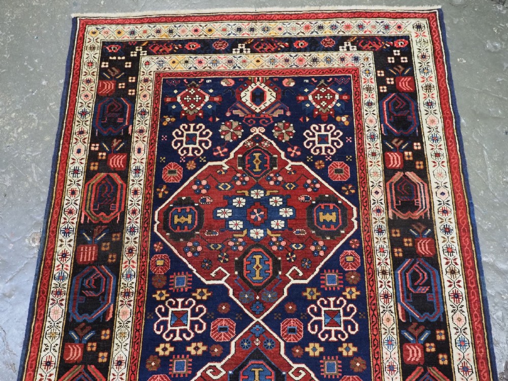 An antique hand-knotted Caucasian Alpan-Kuba runner rug featuring geometric diamond medallions in red and navy blue with detailed ivory borders. View III
