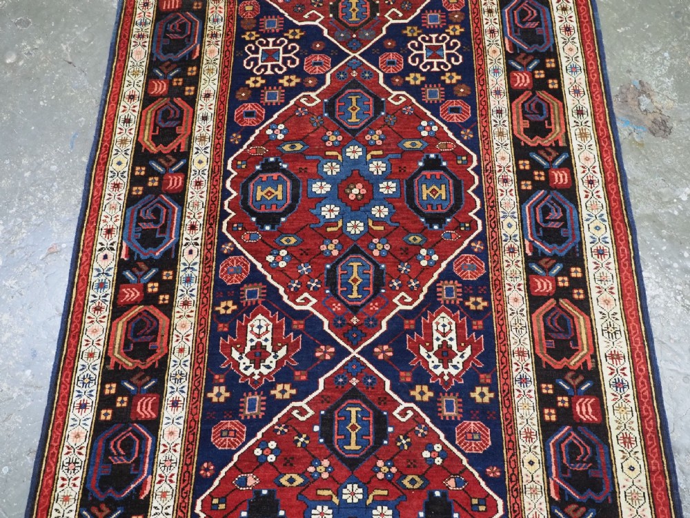 An antique hand-knotted Caucasian Alpan-Kuba runner rug featuring geometric diamond medallions in red and navy blue with detailed ivory borders. View V