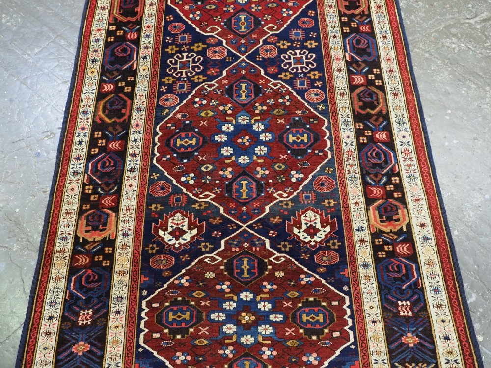 An antique hand-knotted Caucasian Alpan-Kuba runner rug featuring geometric diamond medallions in red and navy blue with detailed ivory borders. View VII