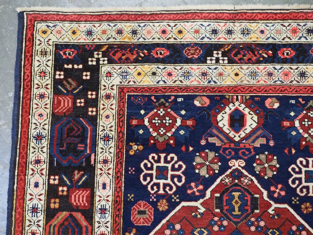 An antique hand-knotted Caucasian Alpan-Kuba runner rug featuring geometric diamond medallions in red and navy blue with detailed ivory borders. View IX