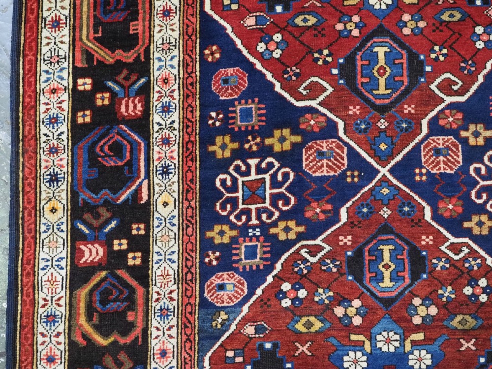 An antique hand-knotted Caucasian Alpan-Kuba runner rug featuring geometric diamond medallions in red and navy blue with detailed ivory borders. View X