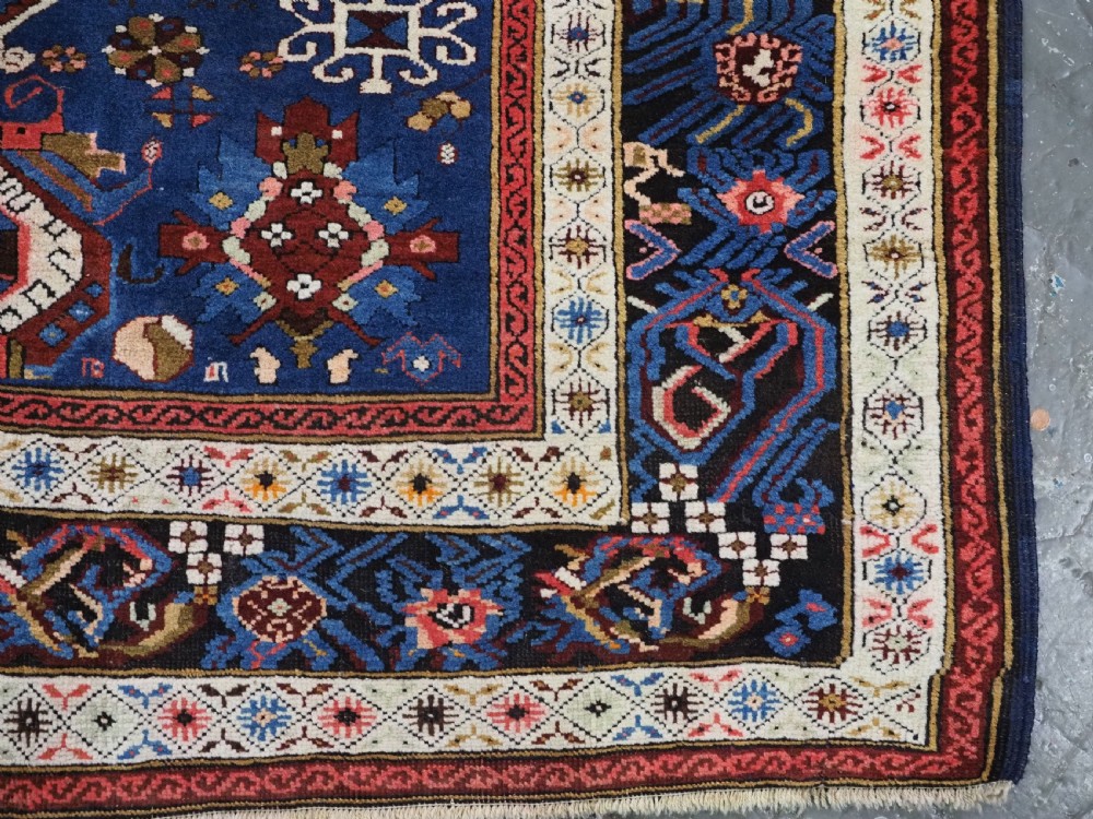 An antique hand-knotted Caucasian Alpan-Kuba runner rug featuring geometric diamond medallions in red and navy blue with detailed ivory borders. View XVIII