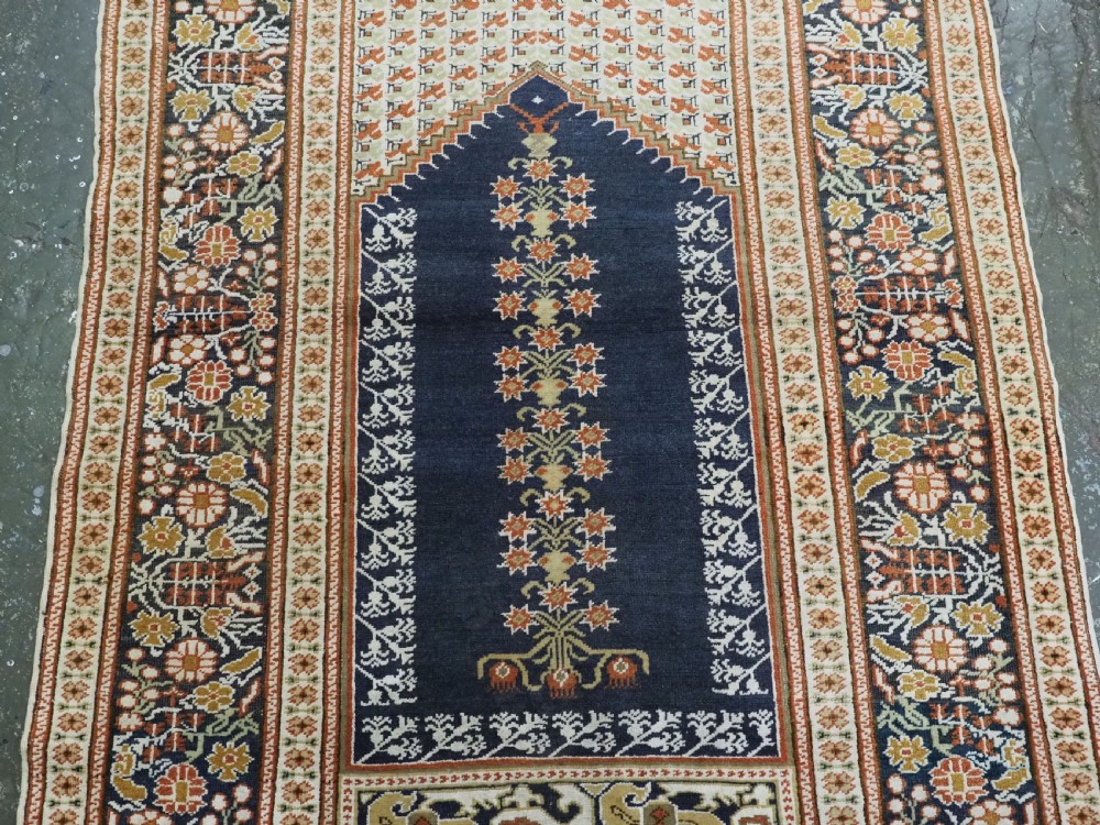 An antique Turkish Panderma hand-knotted wool prayer rug featuring a navy central niche with a floral motif surrounded by detailed ivory and rust geometric floral borders. View V