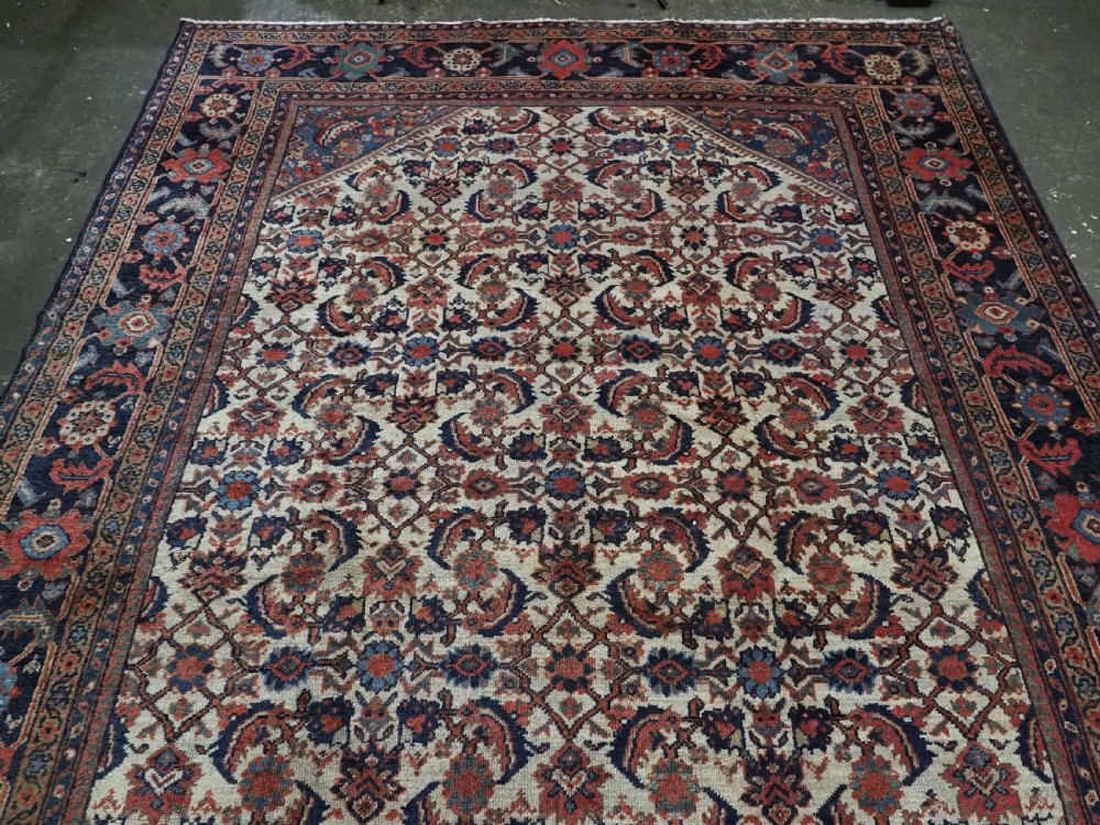 An antique hand-knotted Persian Mahal carpet featuring an ivory central field covered in geometric floral motifs surrounded by dark blue spandrels and a multi-banded border. View III