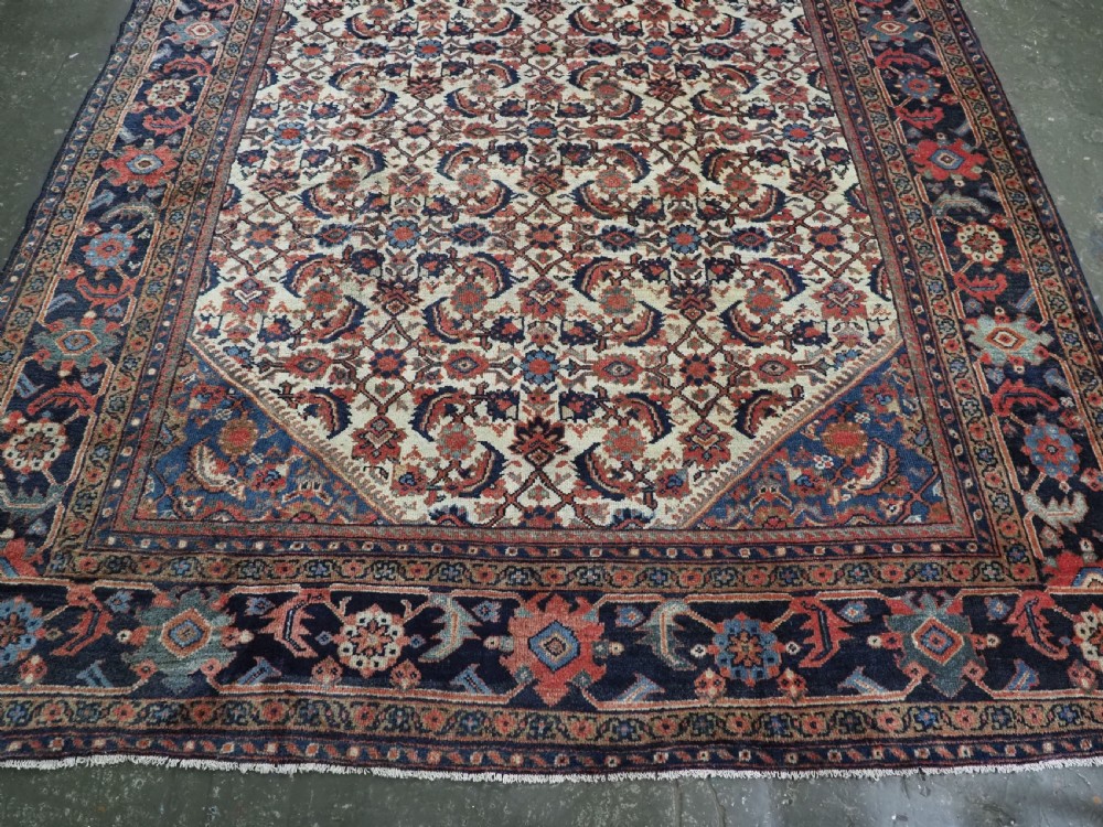An antique hand-knotted Persian Mahal carpet featuring an ivory central field covered in geometric floral motifs surrounded by dark blue spandrels and a multi-banded border. View V