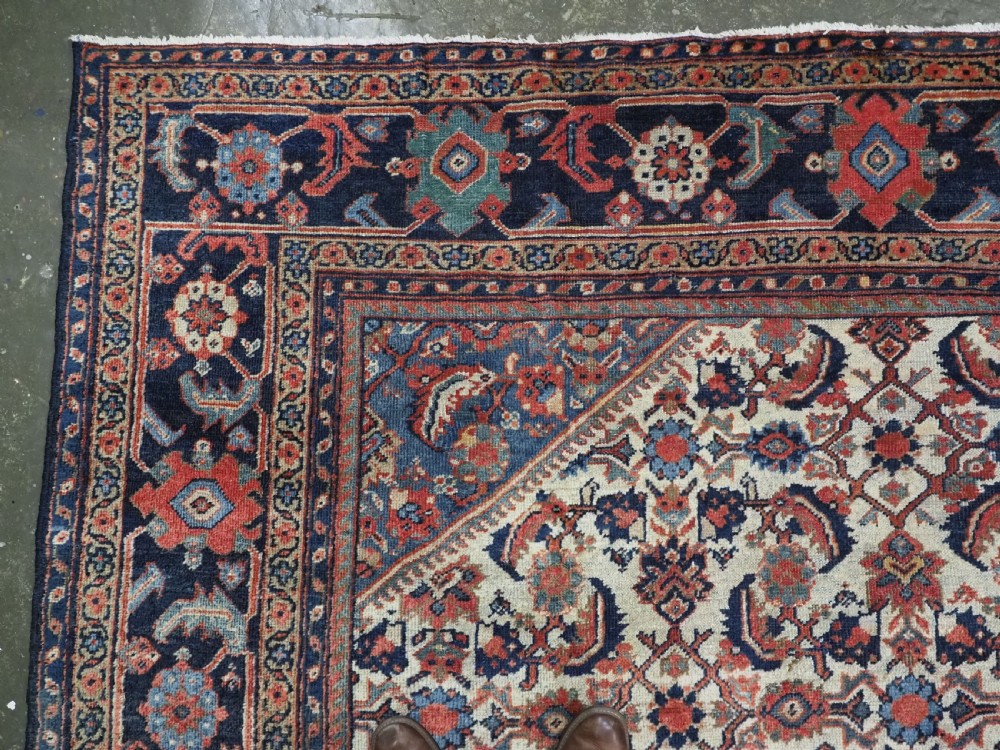 An antique hand-knotted Persian Mahal carpet featuring an ivory central field covered in geometric floral motifs surrounded by dark blue spandrels and a multi-banded border. View VI