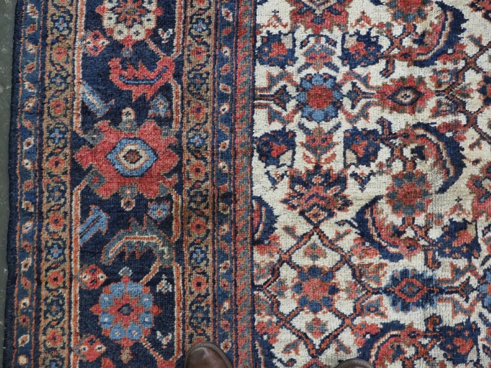 An antique hand-knotted Persian Mahal carpet featuring an ivory central field covered in geometric floral motifs surrounded by dark blue spandrels and a multi-banded border. View VII