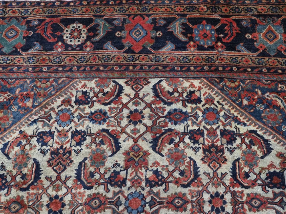 An antique hand-knotted Persian Mahal carpet featuring an ivory central field covered in geometric floral motifs surrounded by dark blue spandrels and a multi-banded border. View IX