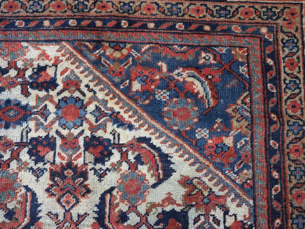 An antique hand-knotted Persian Mahal carpet featuring an ivory central field covered in geometric floral motifs surrounded by dark blue spandrels and a multi-banded border. View X