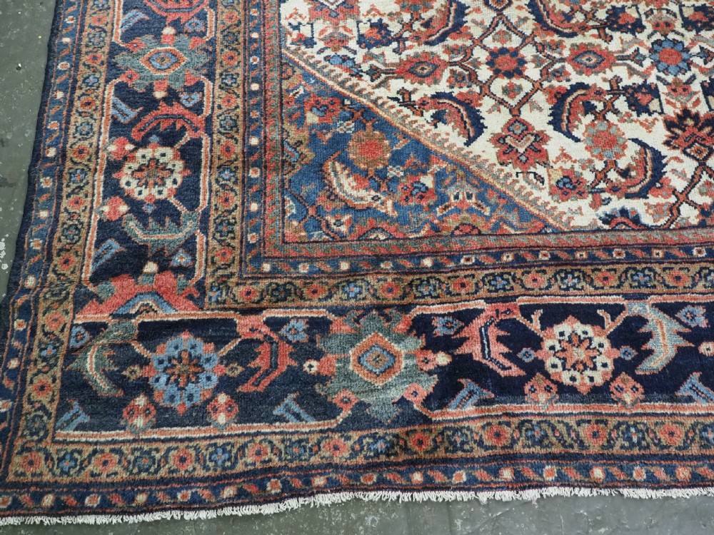 An antique hand-knotted Persian Mahal carpet featuring an ivory central field covered in geometric floral motifs surrounded by dark blue spandrels and a multi-banded border. View XV