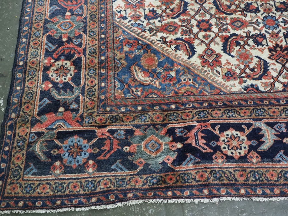 An antique hand-knotted Persian Mahal carpet featuring an ivory central field covered in geometric floral motifs surrounded by dark blue spandrels and a multi-banded border. View XVI