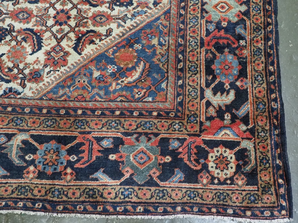 An antique hand-knotted Persian Mahal carpet featuring an ivory central field covered in geometric floral motifs surrounded by dark blue spandrels and a multi-banded border. View XVII