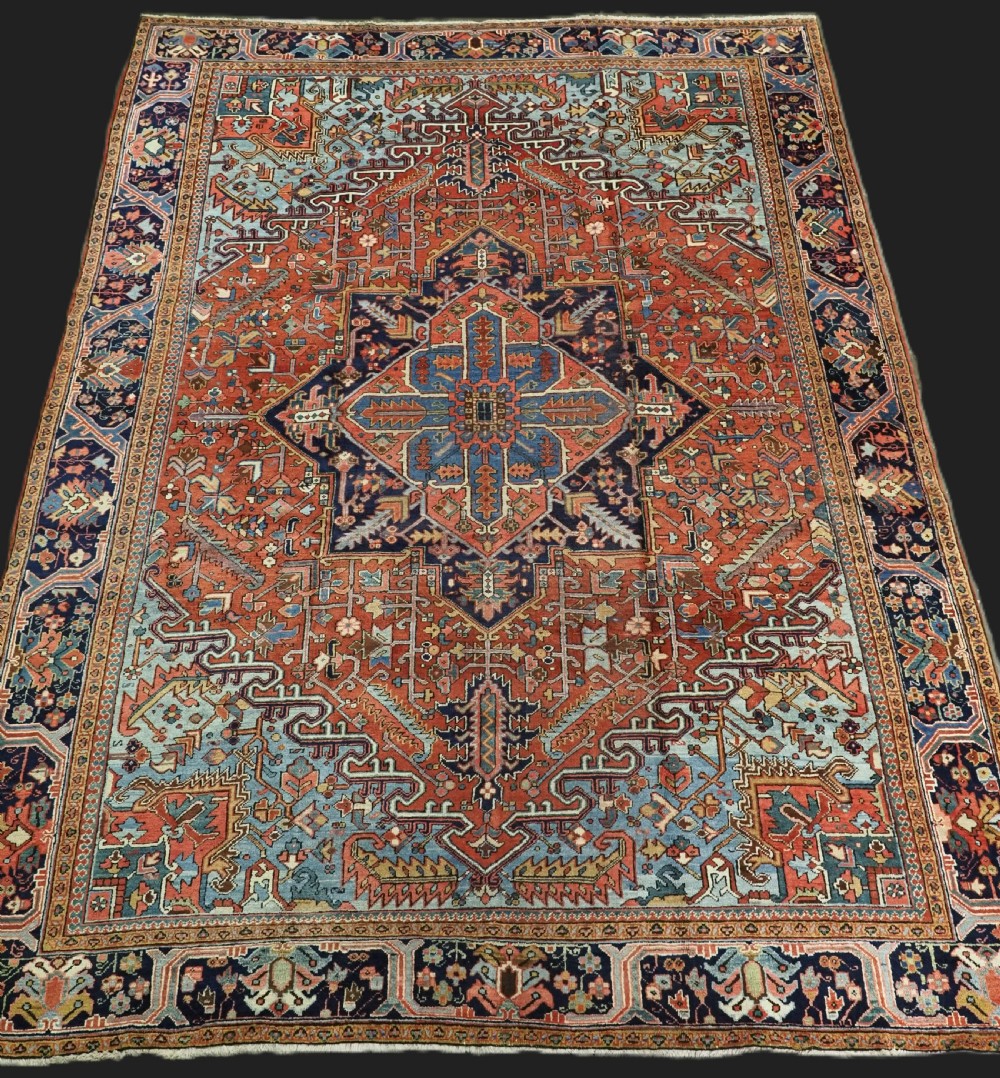 An antique hand-knotted wool Heriz carpet featuring a prominent central geometric star medallion in navy and sky blue surrounded by a terracotta field and stylized borders.