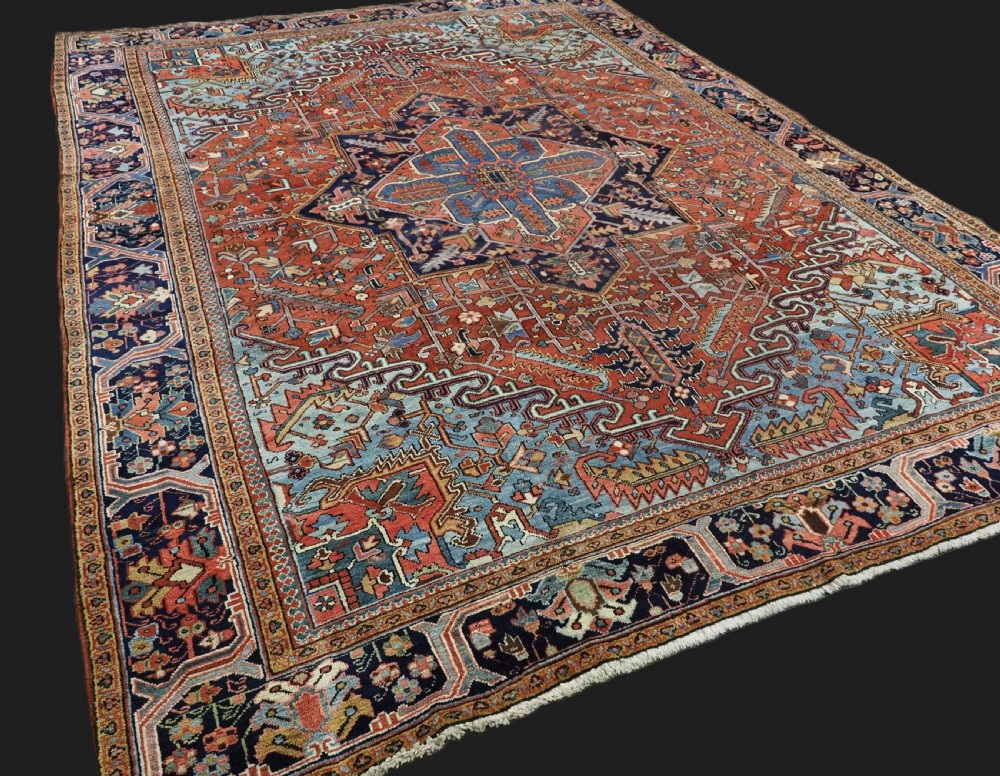 An antique hand-knotted wool Heriz carpet featuring a prominent central geometric star medallion in navy and sky blue surrounded by a terracotta field and stylized borders. View II