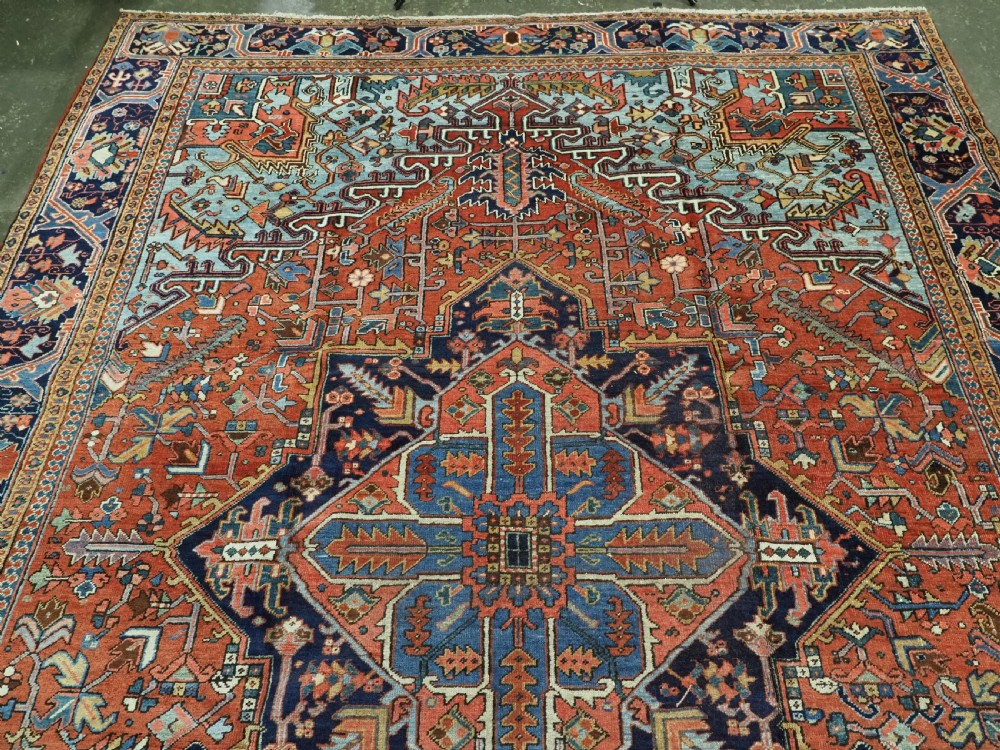 An antique hand-knotted wool Heriz carpet featuring a prominent central geometric star medallion in navy and sky blue surrounded by a terracotta field and stylized borders. View III