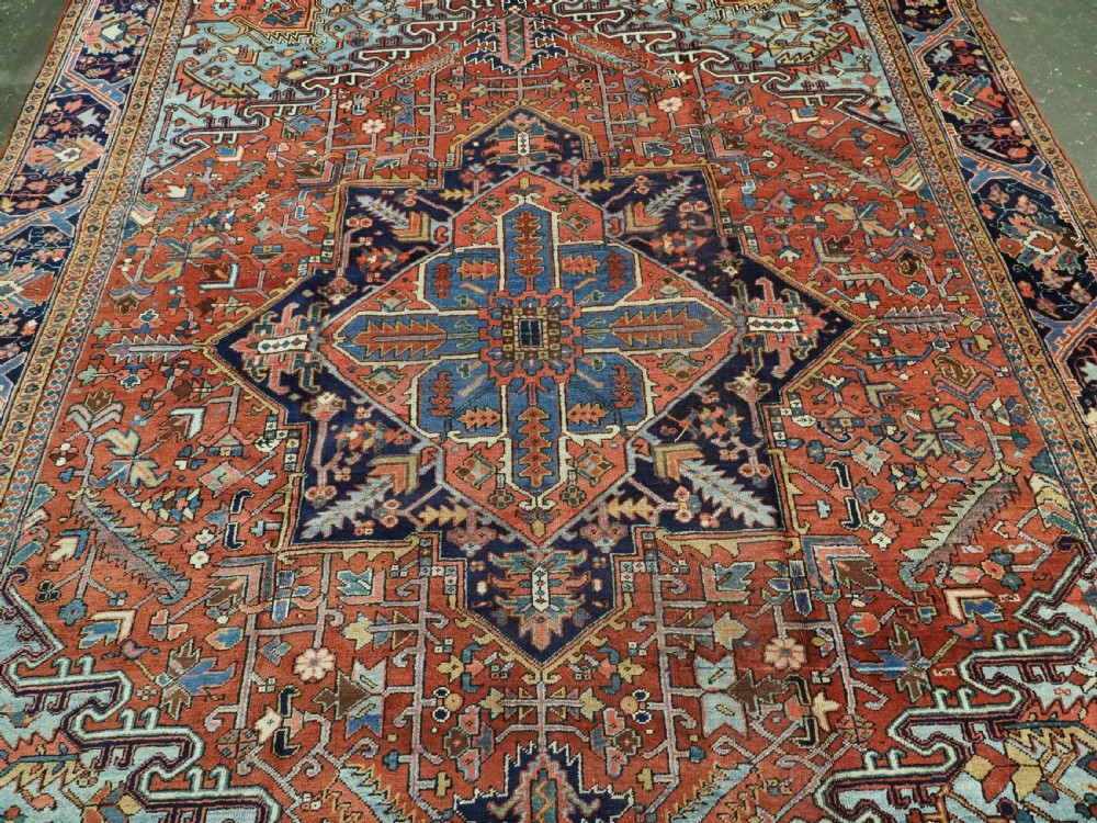 An antique hand-knotted wool Heriz carpet featuring a prominent central geometric star medallion in navy and sky blue surrounded by a terracotta field and stylized borders. View V