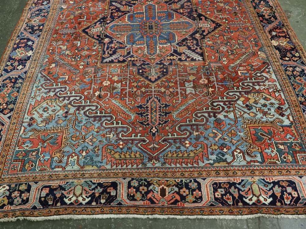 An antique hand-knotted wool Heriz carpet featuring a prominent central geometric star medallion in navy and sky blue surrounded by a terracotta field and stylized borders. View VI