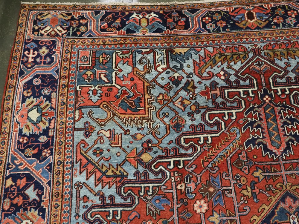 An antique hand-knotted wool Heriz carpet featuring a prominent central geometric star medallion in navy and sky blue surrounded by a terracotta field and stylized borders. View VII