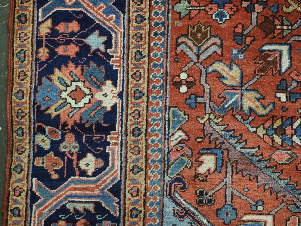 An antique hand-knotted wool Heriz carpet featuring a prominent central geometric star medallion in navy and sky blue surrounded by a terracotta field and stylized borders. View VIII