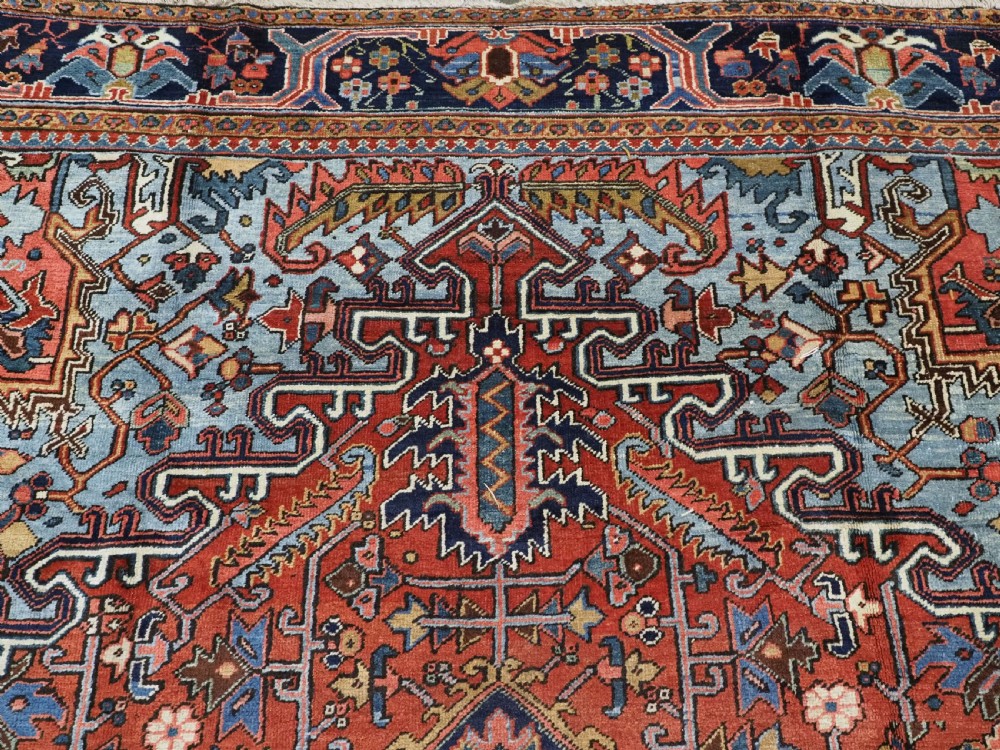 An antique hand-knotted wool Heriz carpet featuring a prominent central geometric star medallion in navy and sky blue surrounded by a terracotta field and stylized borders. View IX
