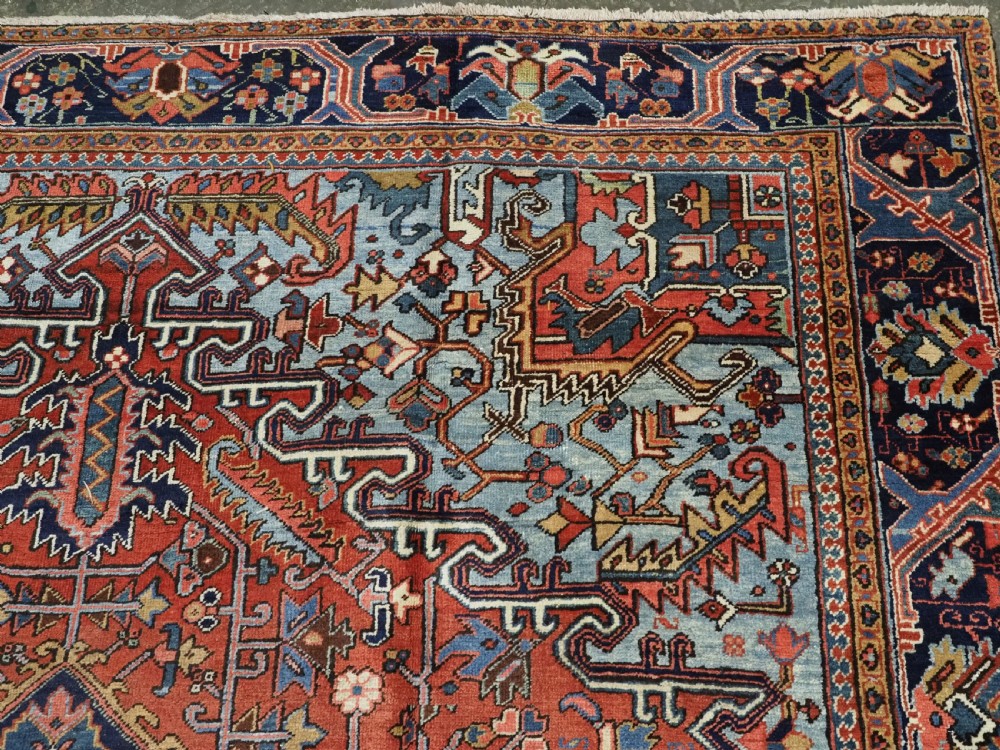 An antique hand-knotted wool Heriz carpet featuring a prominent central geometric star medallion in navy and sky blue surrounded by a terracotta field and stylized borders. View X