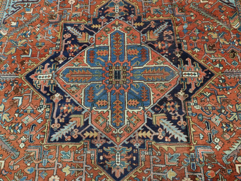 An antique hand-knotted wool Heriz carpet featuring a prominent central geometric star medallion in navy and sky blue surrounded by a terracotta field and stylized borders. View XI
