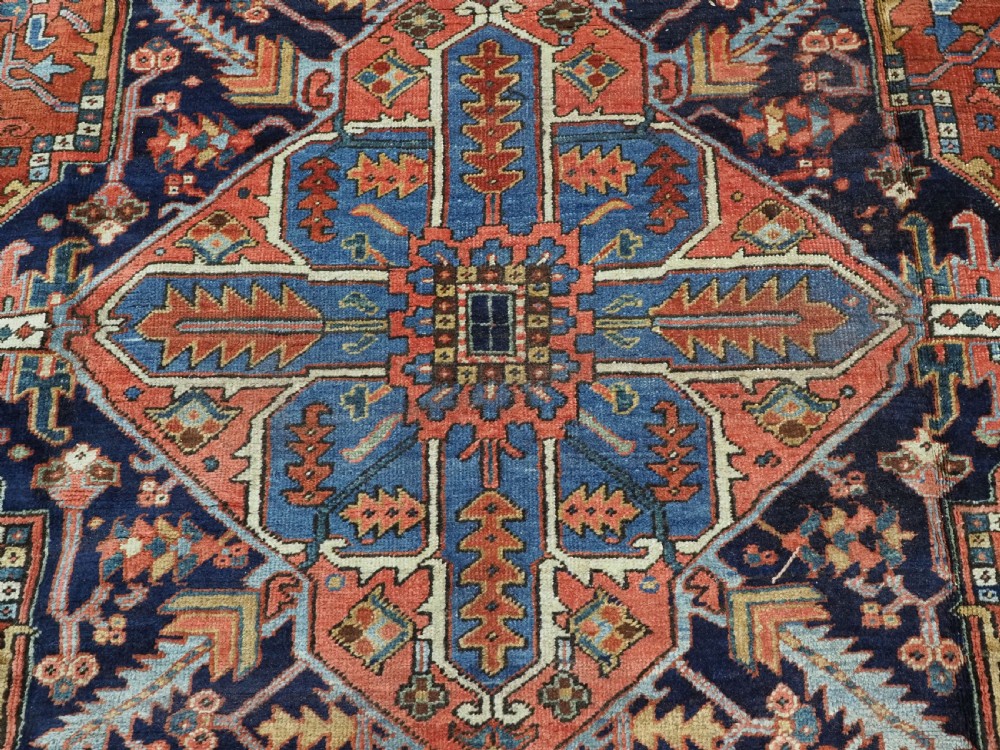 An antique hand-knotted wool Heriz carpet featuring a prominent central geometric star medallion in navy and sky blue surrounded by a terracotta field and stylized borders. View XII