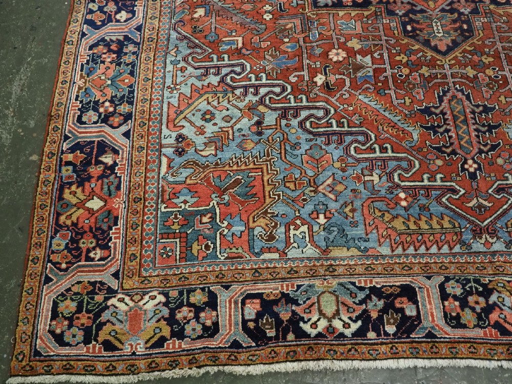 An antique hand-knotted wool Heriz carpet featuring a prominent central geometric star medallion in navy and sky blue surrounded by a terracotta field and stylized borders. View XIV