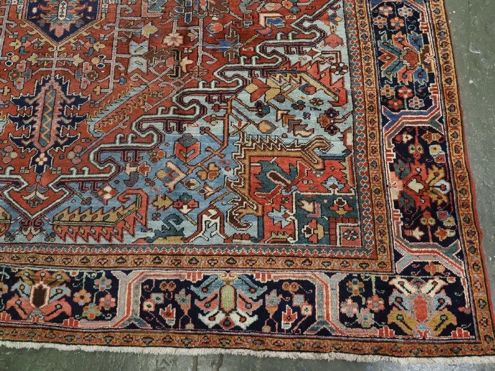 An antique hand-knotted wool Heriz carpet featuring a prominent central geometric star medallion in navy and sky blue surrounded by a terracotta field and stylized borders. View XV