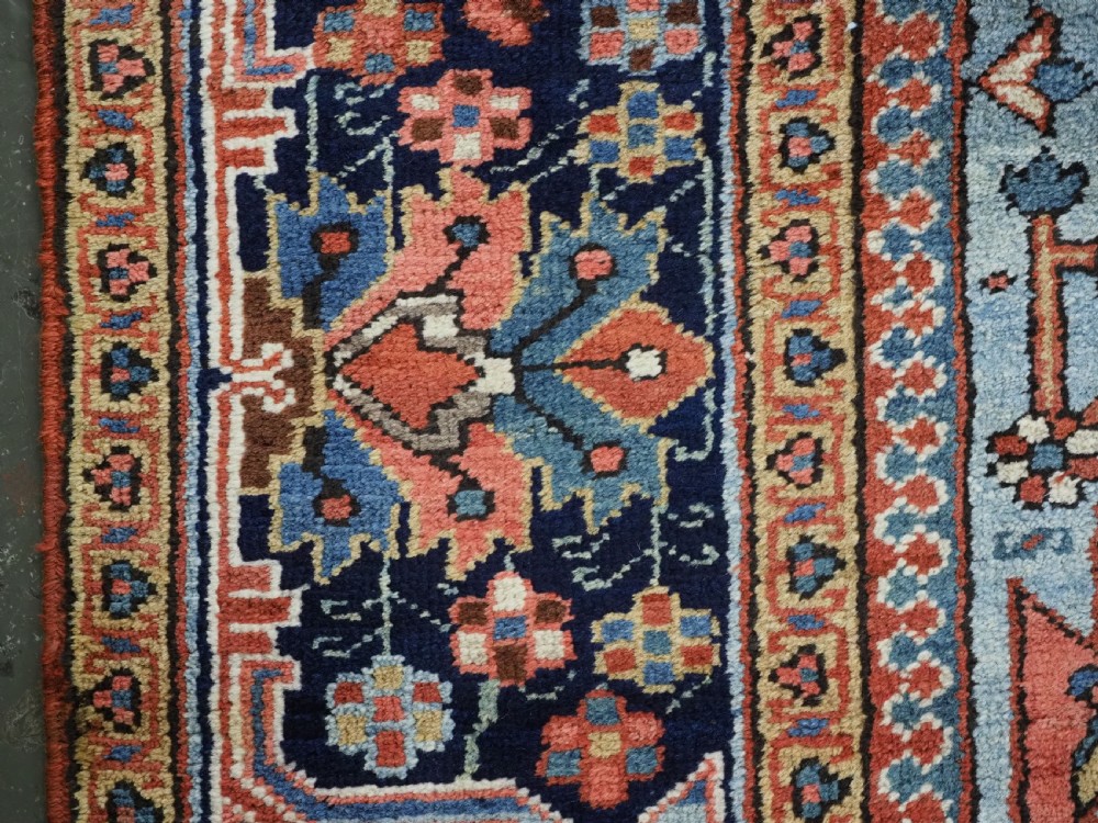 An antique hand-knotted wool Heriz carpet featuring a prominent central geometric star medallion in navy and sky blue surrounded by a terracotta field and stylized borders. View XVII