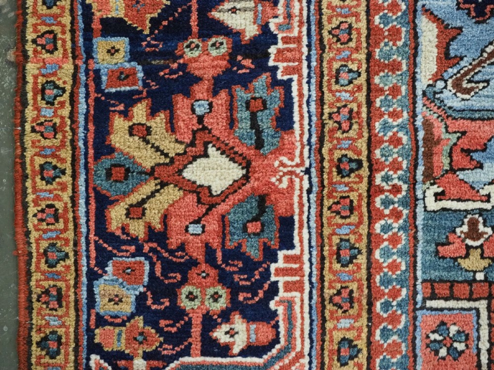An antique hand-knotted wool Heriz carpet featuring a prominent central geometric star medallion in navy and sky blue surrounded by a terracotta field and stylized borders. View XVIII