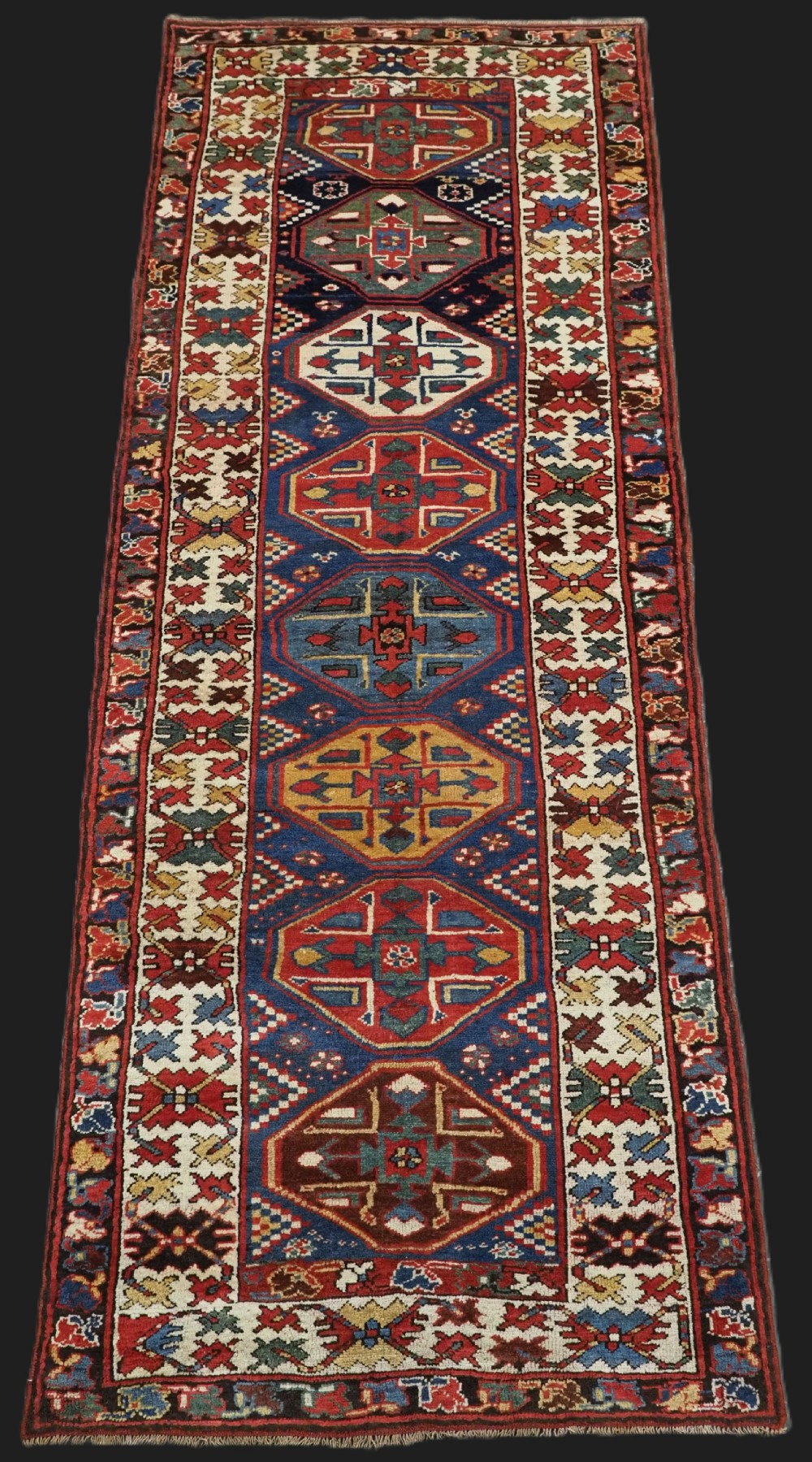 An antique hand-knotted Caucasian wool runner rug featuring a sequence of geometric diamond medallions on an indigo blue field surrounded by patterned borders.