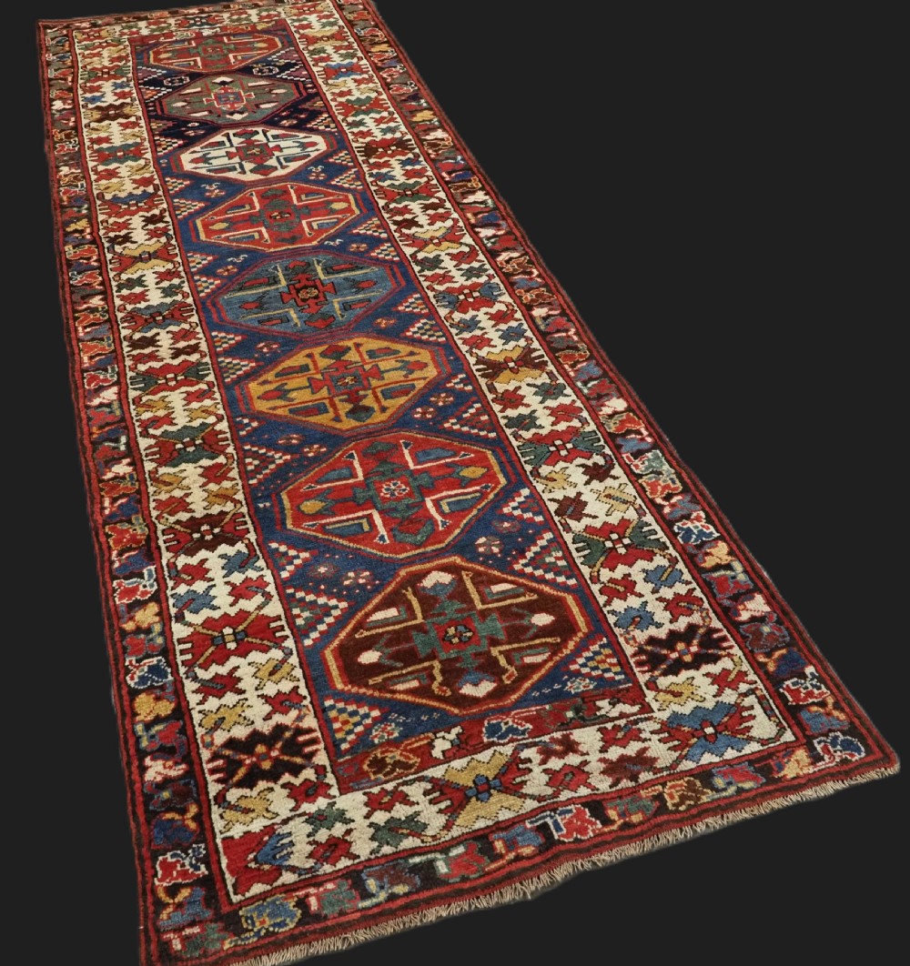 An antique hand-knotted Caucasian wool runner rug featuring a sequence of geometric diamond medallions on an indigo blue field surrounded by patterned borders. View II