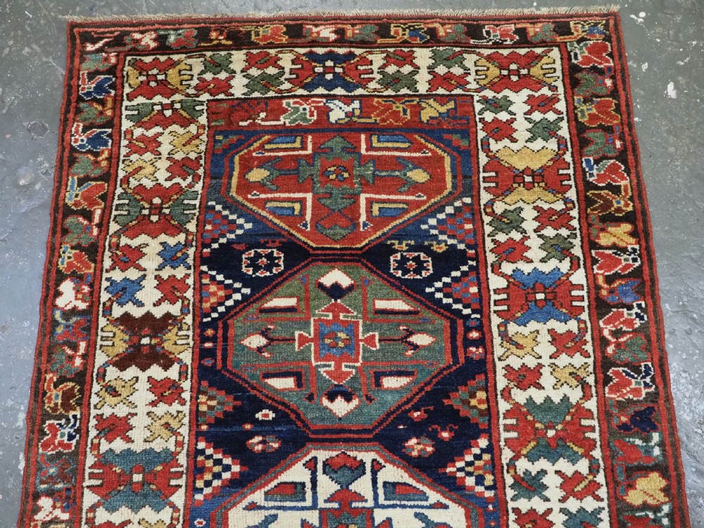 An antique hand-knotted Caucasian wool runner rug featuring a sequence of geometric diamond medallions on an indigo blue field surrounded by patterned borders. View III