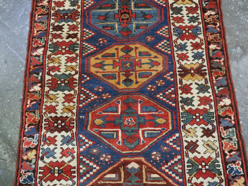 An antique hand-knotted Caucasian wool runner rug featuring a sequence of geometric diamond medallions on an indigo blue field surrounded by patterned borders. View VI