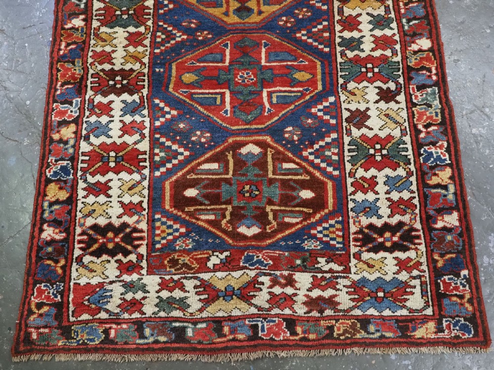 An antique hand-knotted Caucasian wool runner rug featuring a sequence of geometric diamond medallions on an indigo blue field surrounded by patterned borders. View VII