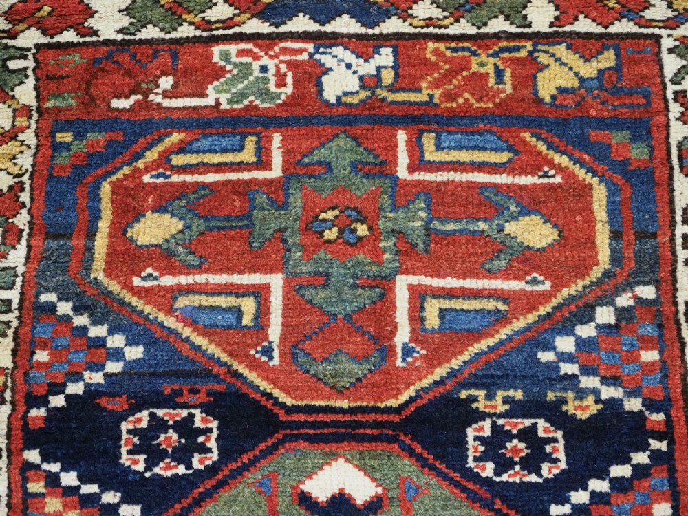 An antique hand-knotted Caucasian wool runner rug featuring a sequence of geometric diamond medallions on an indigo blue field surrounded by patterned borders. View X