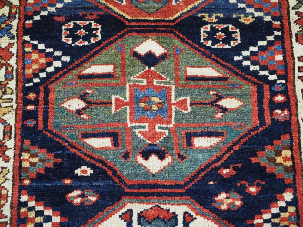 An antique hand-knotted Caucasian wool runner rug featuring a sequence of geometric diamond medallions on an indigo blue field surrounded by patterned borders. View XI