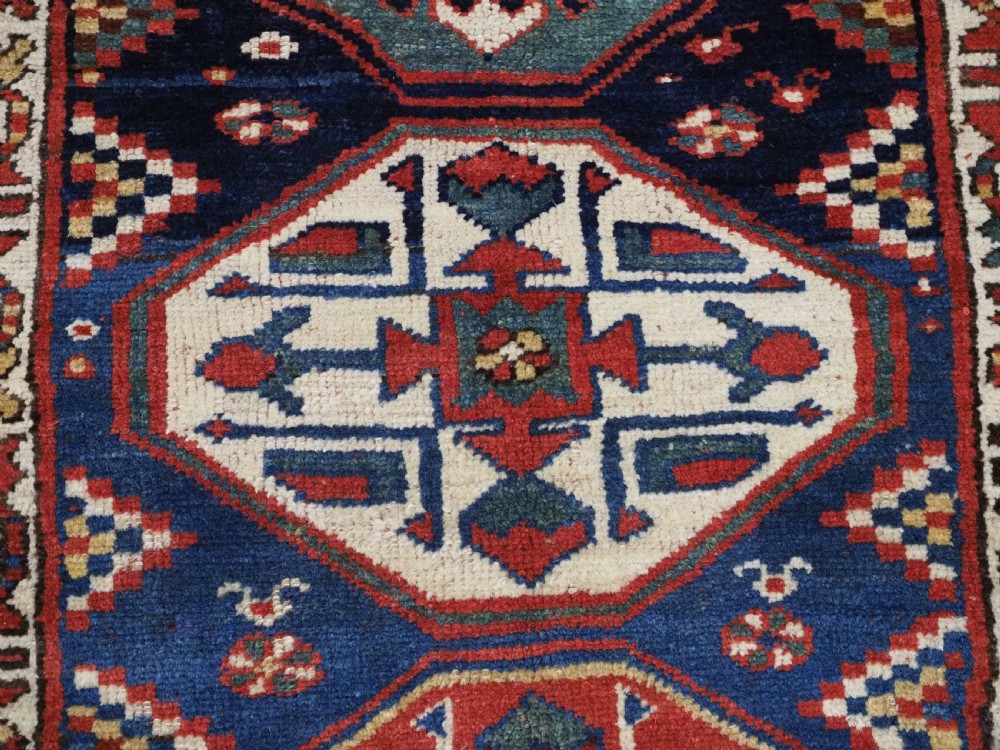 An antique hand-knotted Caucasian wool runner rug featuring a sequence of geometric diamond medallions on an indigo blue field surrounded by patterned borders. View XII